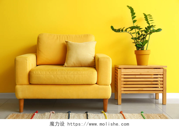 黄色背景前的黄色沙发和木制柜子彩墙附近桌子上舒适的扶手椅和室内盆栽